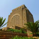 Voortrekker Monument brick tower with ornate geometric patterns and decorative windows, surrounded by palm trees and garden w